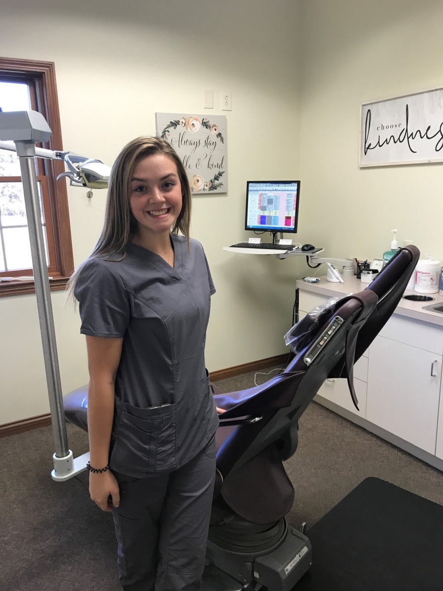 girl wearing scrubs next to dental chair